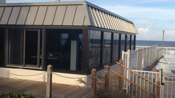 A modern building with large glass windows, a wooden deck, and a view of the sea. - 1 Bdrm..2026 Year-round time slots ..great View & Reviews...on the no drive sand (New Smyrna Beach)