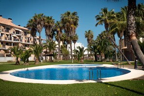 A swimming pool surrounded by palm trees and a building with balconies.