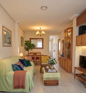 A living room with a sofa, a coffee table, a dining area with chairs, a TV stand, and a cabinet. - Fully furnished vacation rental with Wi-Fi, 150 meters from Les Bovetes Beach (Denia, Alicante)