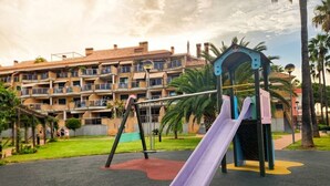 A playground with a slide and swings, set against a backdrop of a residential building.