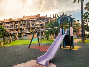 A playground with a slide and swings, set against a backdrop of a residential building. - Fully furnished vacation rental with Wi-Fi, 150 meters from Les Bovetes Beach (Denia, Alicante)