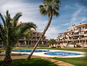 A resort with a swimming pool, palm trees, and multi-story buildings with balconies.