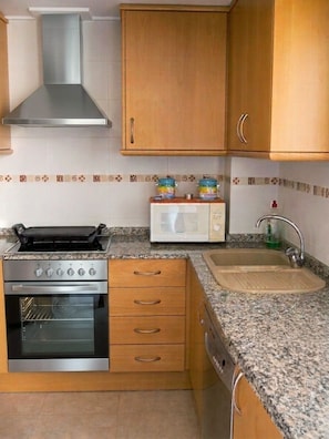 A compact kitchen with a stove, oven, microwave, and a sink. - Fully furnished vacation rental with Wi-Fi, 150 meters from Les Bovetes Beach (Denia, Alicante)