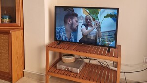 Televisio on sijoitettu puiseen jalustaan, ja sen yläpuolella on punottu kaappi.