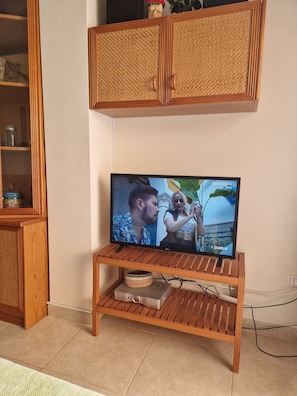 Un téléviseur posé sur un meuble en bois, avec une armoire en osier au-dessus.