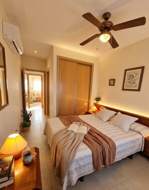 A hotel room with a bed, bedside table, lamp, and ceiling fan. - Fully furnished vacation rental with Wi-Fi, 150 meters from Les Bovetes Beach (Denia)