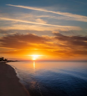 Un coucher de soleil sur une mer calme, avec une plage sur la gauche.