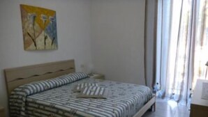 Un dormitorio con cama, mesita de noche, un cuadro en la pared y una ventana con cortinas.