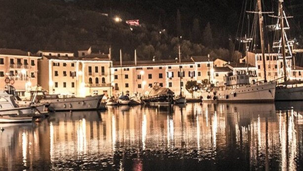 Un puerto deportivo con barcos amarrados, edificios iluminados y una colina al fondo.
