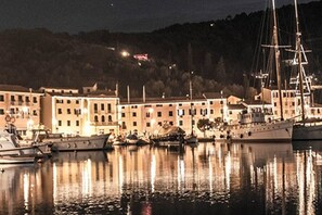 Uma marina com barcos atracados, edifícios iluminados e uma colina ao fundo.
