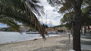 Una playa con una palmera, un balde blanco y un muelle con barcos.