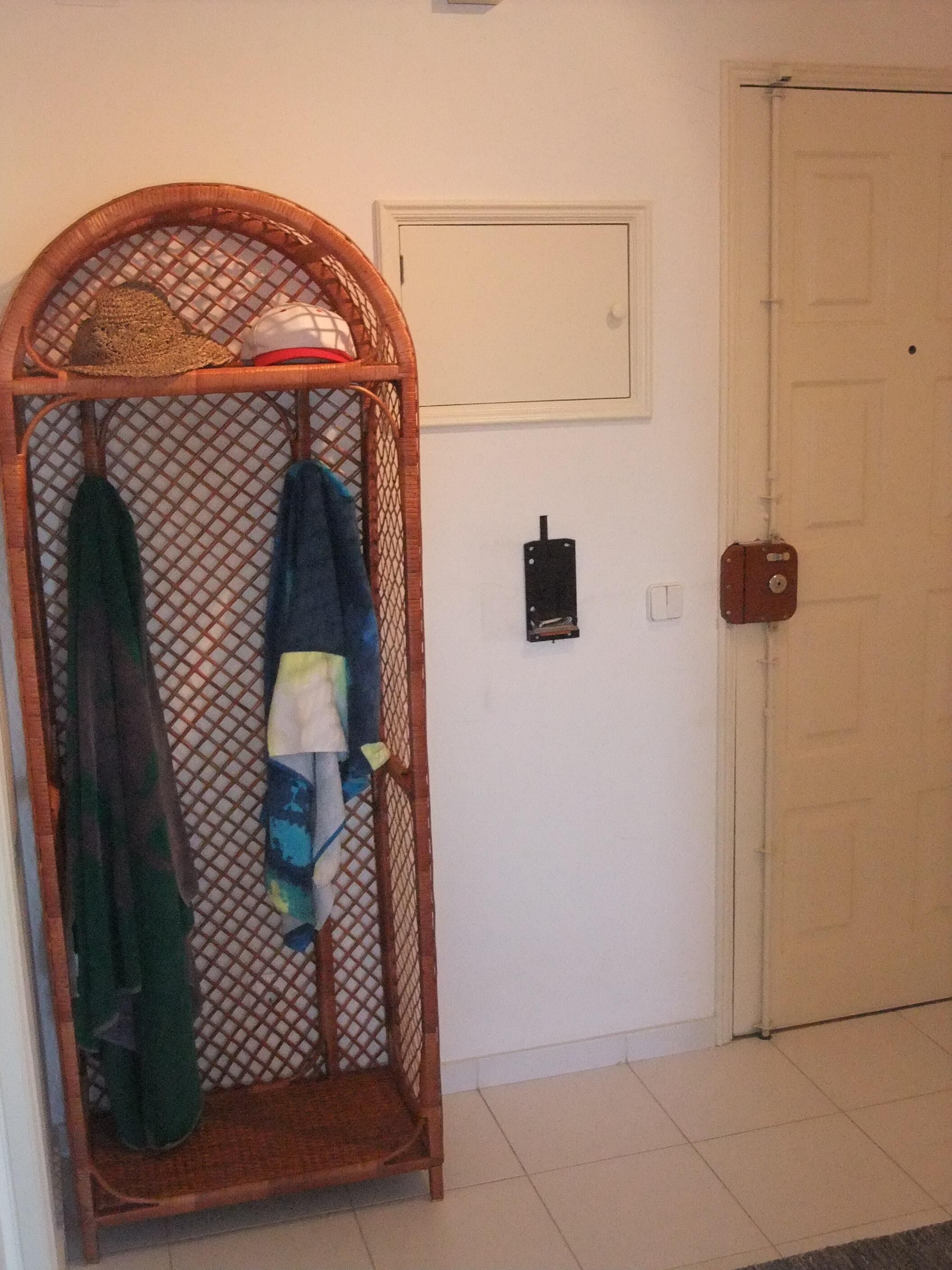 Une pièce avec un étendoir en bois à arc, une porte blanche, une boîte électrique fixée au mur et un sol carrelé.