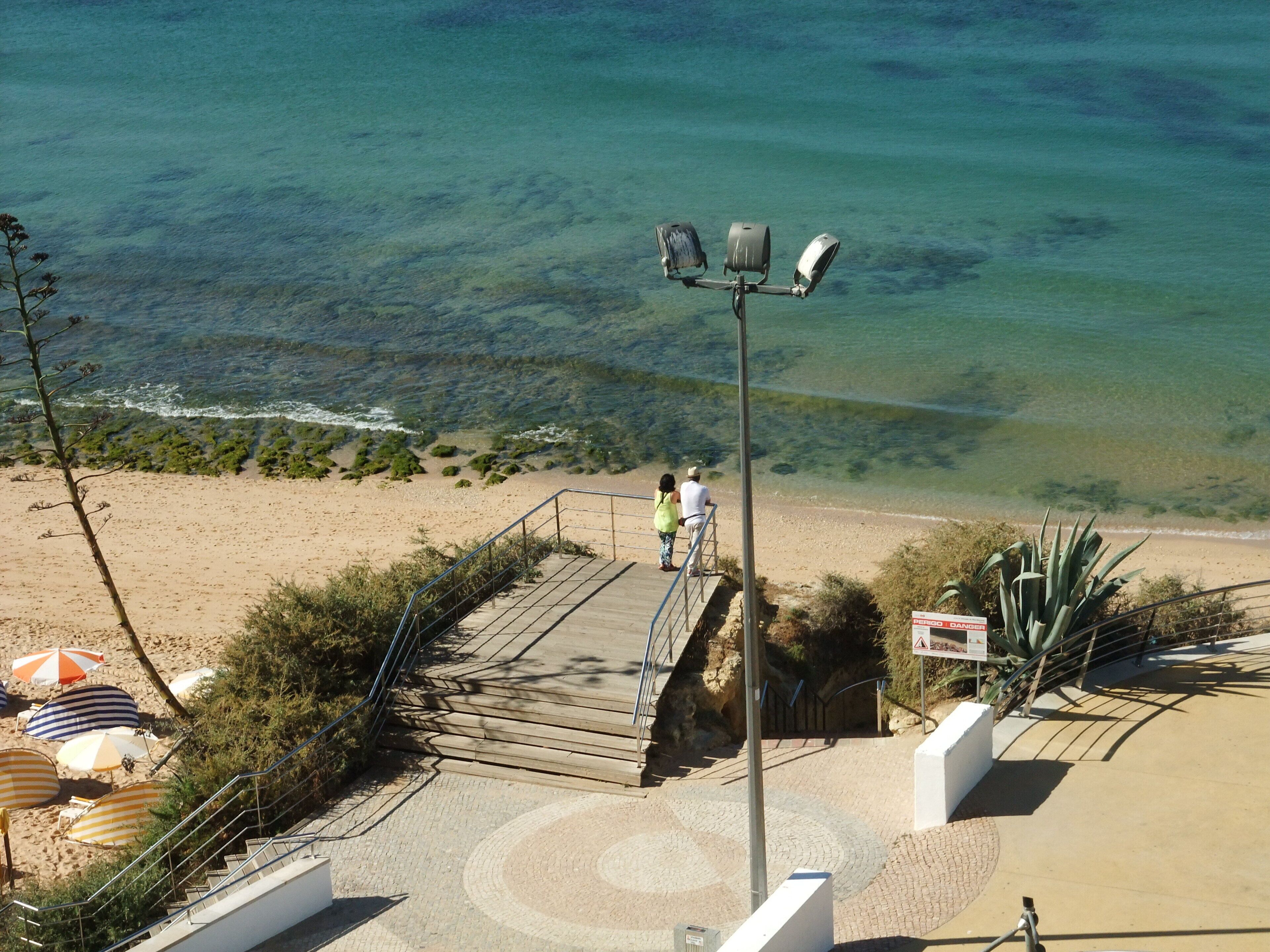 A beachside walkway with a clear view of the ocean, a few people walking, and beach umbrellas.
