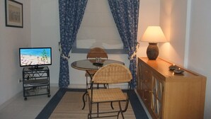 Ein kleines Zimmer mit Fernseher, einem Tisch mit Stühlen, einer Lampe und einem Schrank.