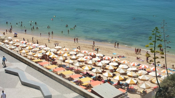 Ein Strand mit vielen Sonnenschirmen und Menschen, die das Wasser genießen.