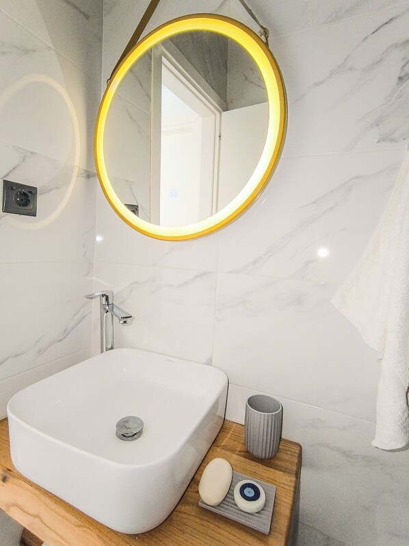 A bathroom with a white marble sink, a round mirror with a yellow frame, and a wooden vanity.