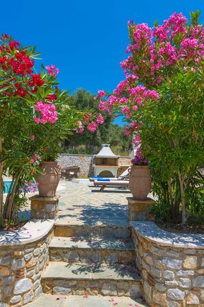 A stone pathway leading to a pool area with a barbecue setup and outdoor seating.