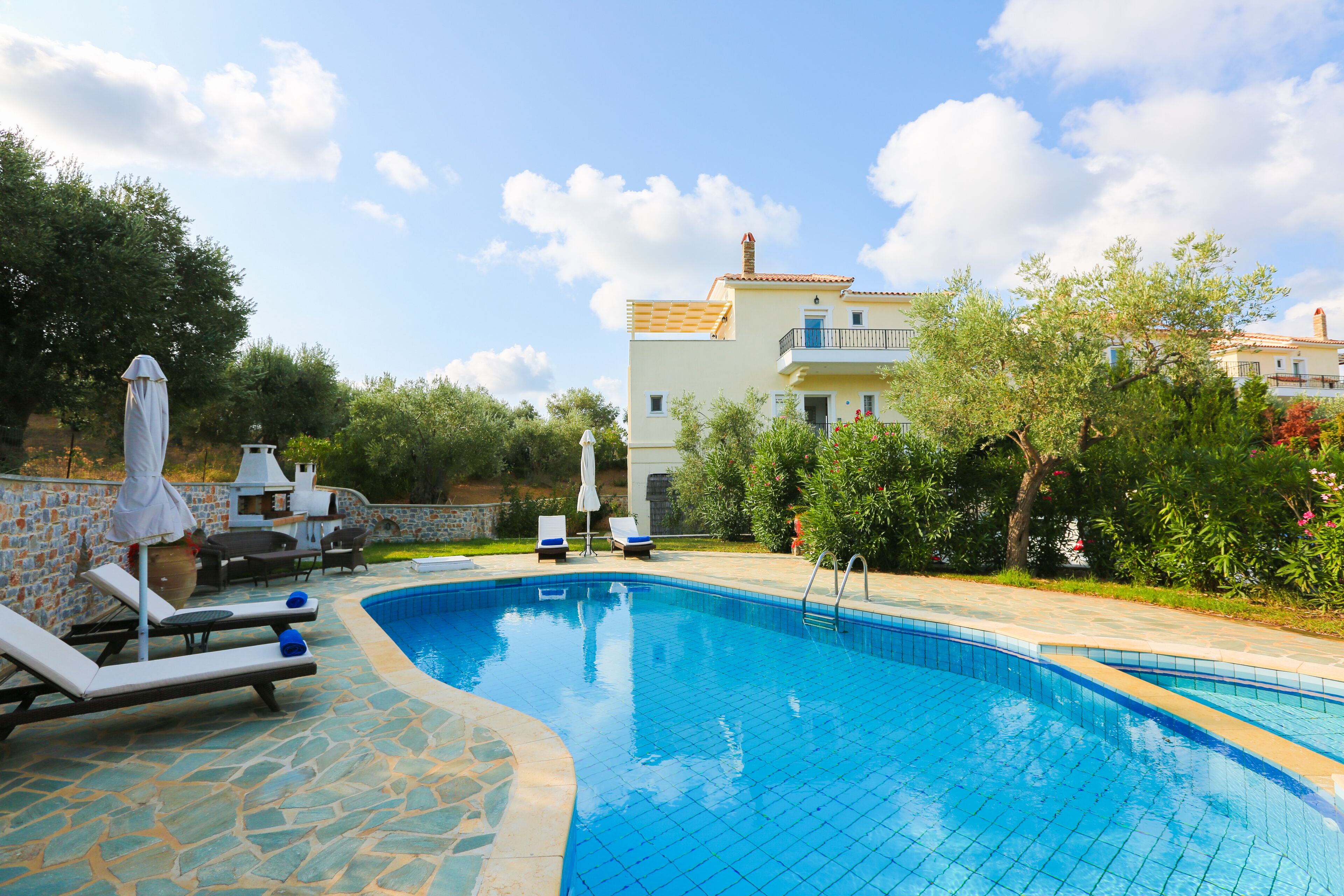 A swimming pool with lounge chairs, a stone patio, and a two-story building in the background.