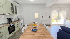 A modern kitchen with white cabinets, a wooden dining table, and a blue sofa in the living area. - Luxurious and family friendly villa with large private pool 5 mins from Skiathos (Skiathos)