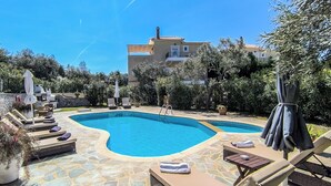 A swimming pool with lounge chairs and umbrellas, surrounded by stone tiles and greenery. - Luxurious and family friendly villa with large private pool 5 mins from Skiathos (Skiathos)
