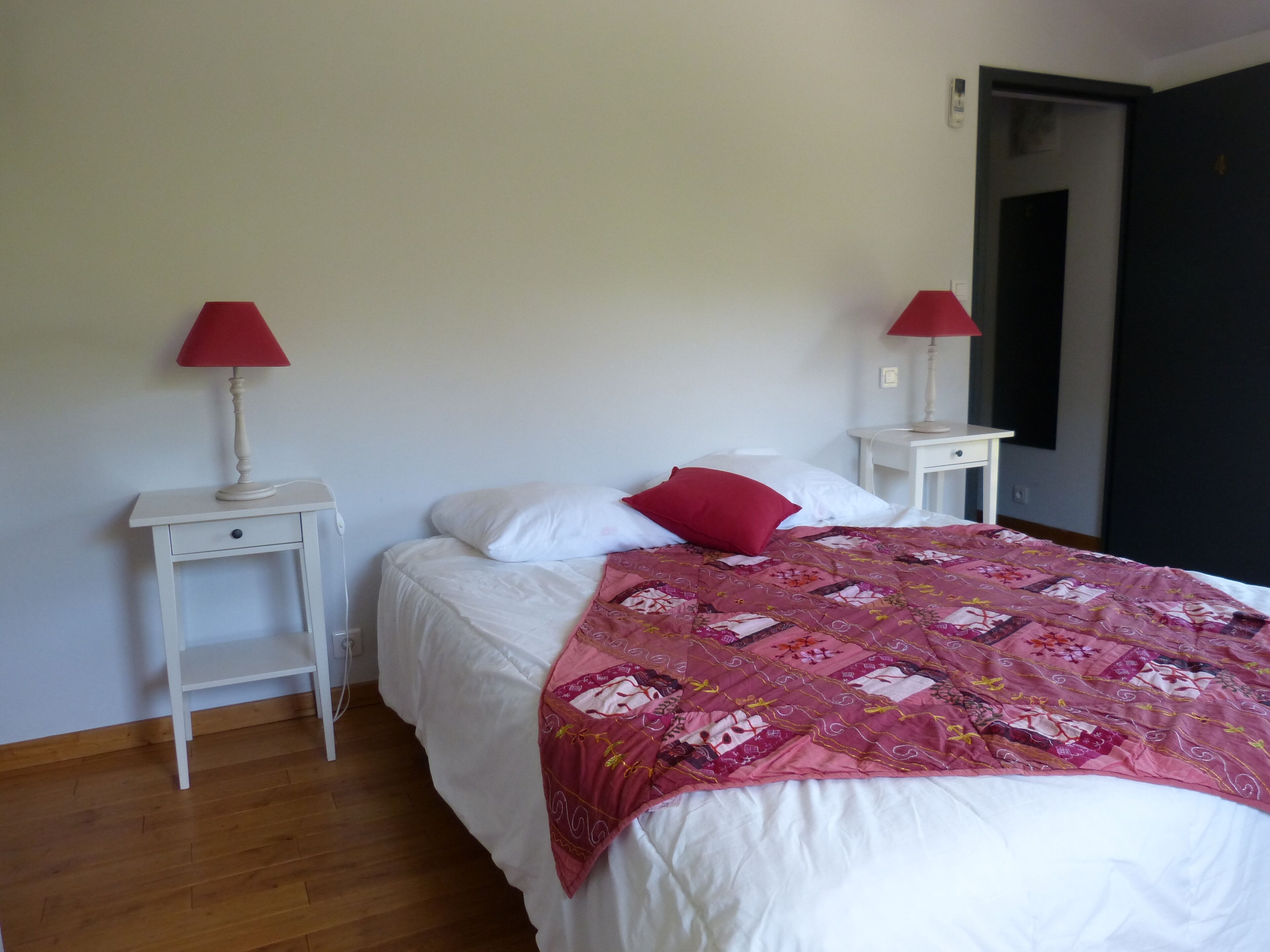 Un dormitorio con una cama, dos mesitas de noche y dos lámparas rojas.