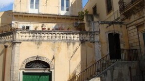 Un immeuble de deux étages avec une porte verte, un balcon orné de plantes en pot et une balustrade en pierre.