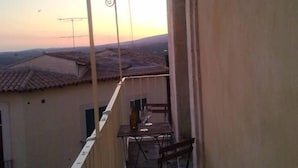 Un balcon avec une table et des chaises, donnant sur un quartier résidentiel aux toits recouverts de tuiles.
