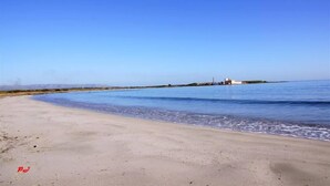 Une plage avec un ciel dégagé, une eau calme et une structure visible au loin.