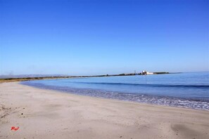 Ein Strand mit blauem Himmel, ruhigem Wasser und einer entfernten Bebauung.