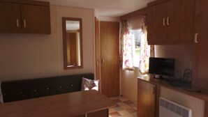 Una cucina compatta con mobili in legno, un piccolo frigorifero, un televisore e una finestra con tende floreali.