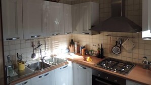 Een keuken met witte kasten, een roestvrijstalen spoelbak, een gasfornuis en een hangende kruidenrek.
