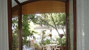 Een open patio met wicker meubilair, een glazen deur naar buiten en uitzicht op de tuin.