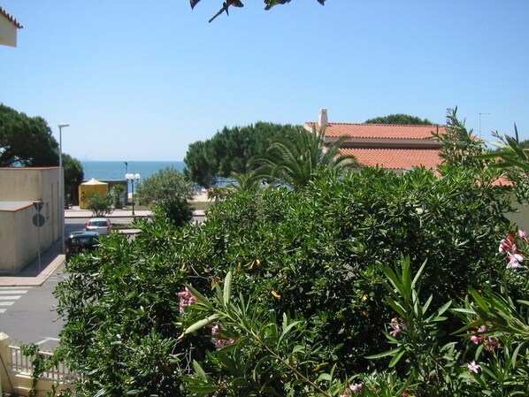A coastal view with a building featuring a red-tiled roof, lush greenery, and a clear sky.