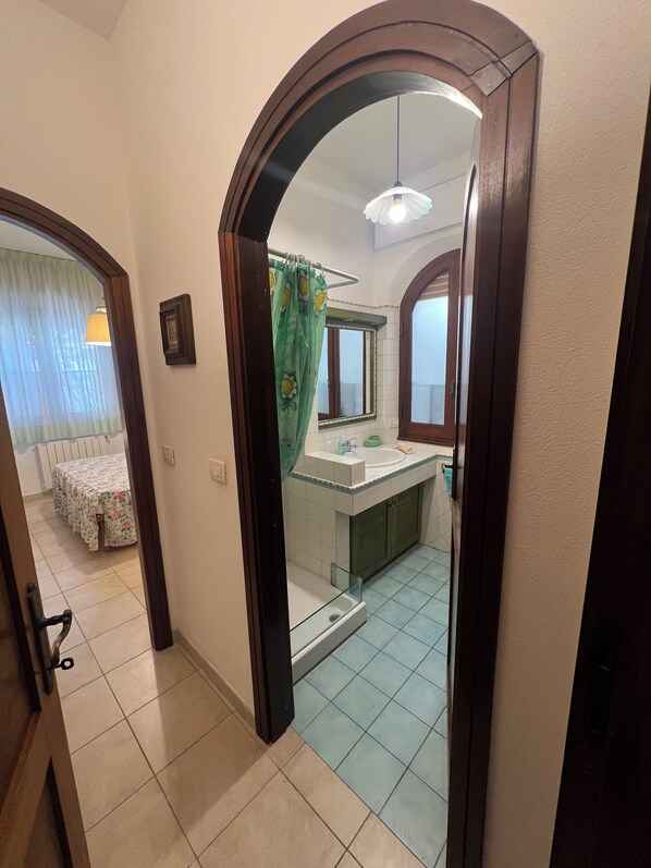 Un pasillo que lleva a un baño con lavamanos, espejo y cortina de ducha.