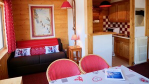 A cozy room with a wooden interior, a sofa with red cushions, a dining table with chairs, and a kitchen area with wooden cabinets and a checkered backsplash. - COURCHEVEL 1850 RESIDENCE CHALET STYLE - BEAUTIFUL VIEW ON MASSIF DE LA VANOISE (Courchevel)