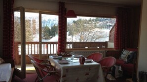 A dining area with a table set for two, red wicker chairs, a view of a snowy landscape through large windows, and a red lamp on the table. - COURCHEVEL 1850 RESIDENCE CHALET STYLE - BEAUTIFUL VIEW ON MASSIF DE LA VANOISE (Courchevel)