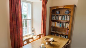 Een eethoek met een houten tafel, stoelen, een houten boekenkast en een raam met gordijnen.