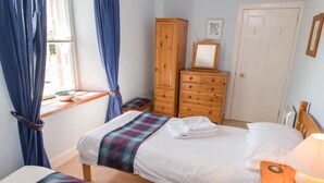 Een slaapkamer met twee bedden, een houten garderobe, een nachtkastje met een lamp en een raam met gordijnen.