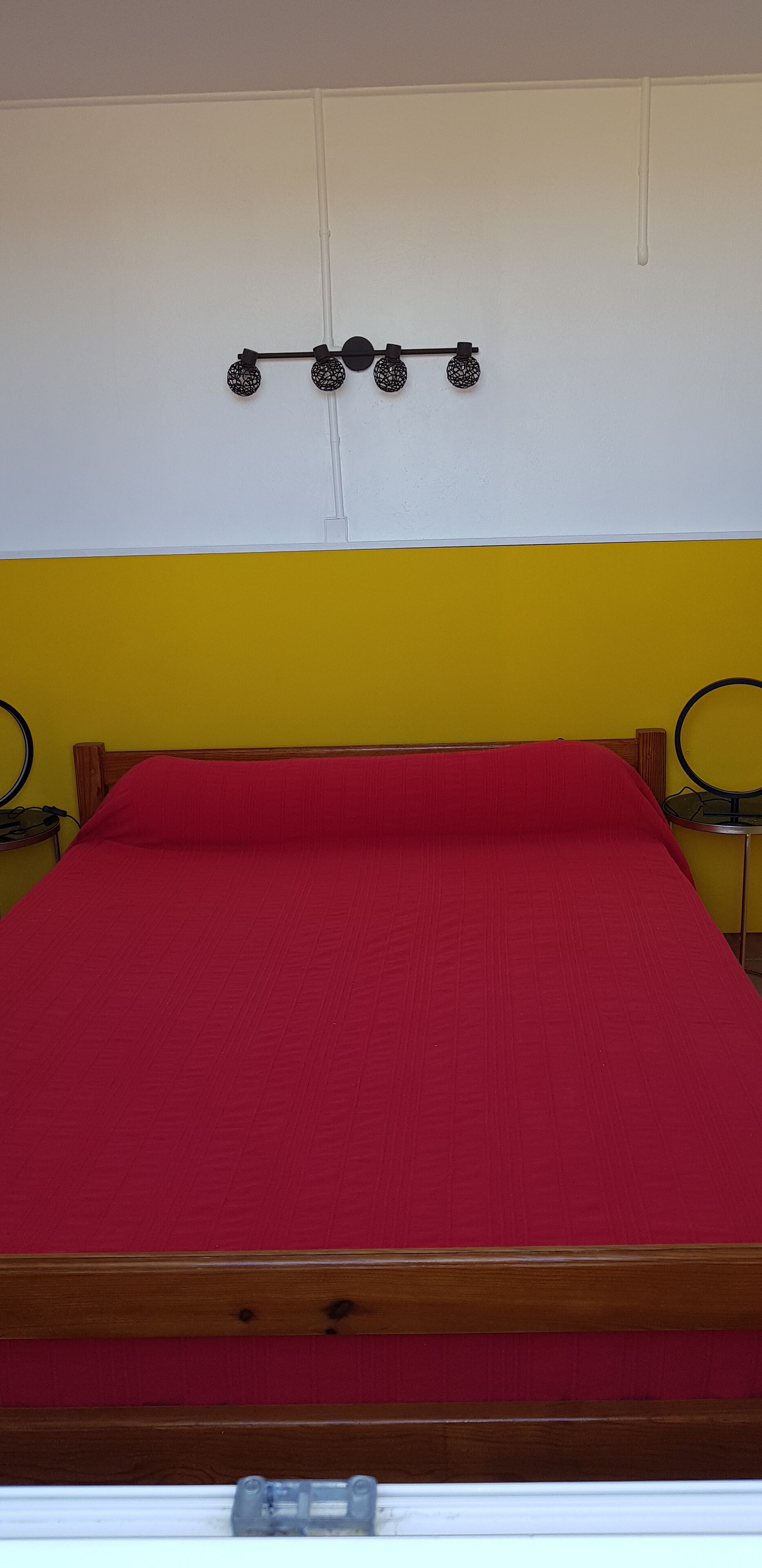 Ein Bett mit roter Matratze, einem Holz-Kopfteil und einer gelben Wand mit weißer Decke.