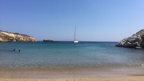 A beach with clear water, rocky cliffs, and a sailboat.