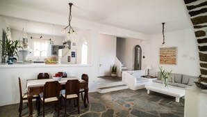 A spacious living area with a stone floor, a dining table with chairs, a white sofa, and a kitchen in the background.