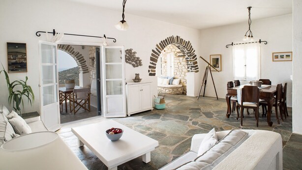 A spacious living area with a stone floor, white furniture, and a view through an open door.