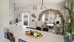 A modern kitchen with a white countertop, a fruit basket, and a view of the living area.