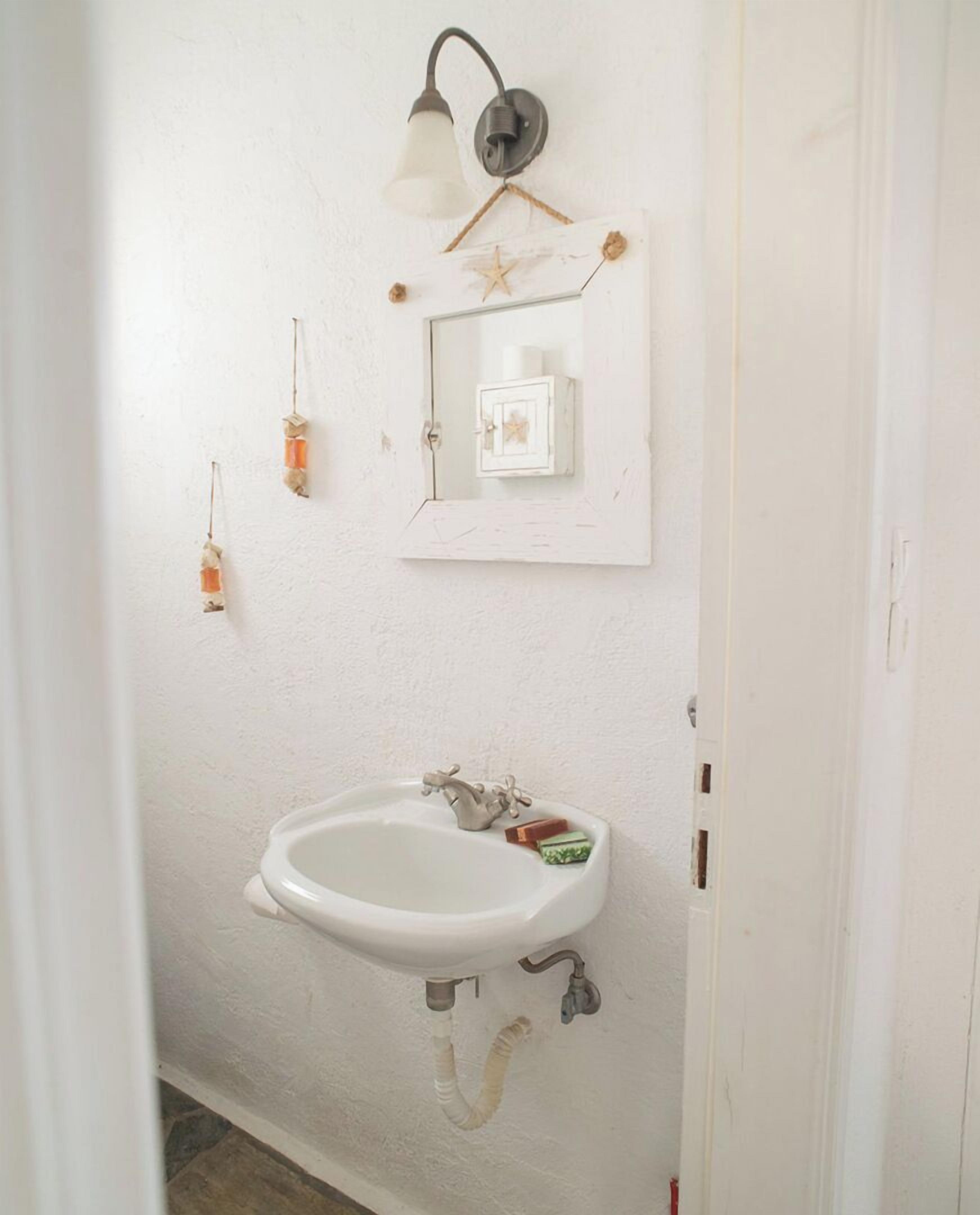 Une salle de bain avec un lavabo blanc, un luminaire fixé au mur et un petit objet décoratif.