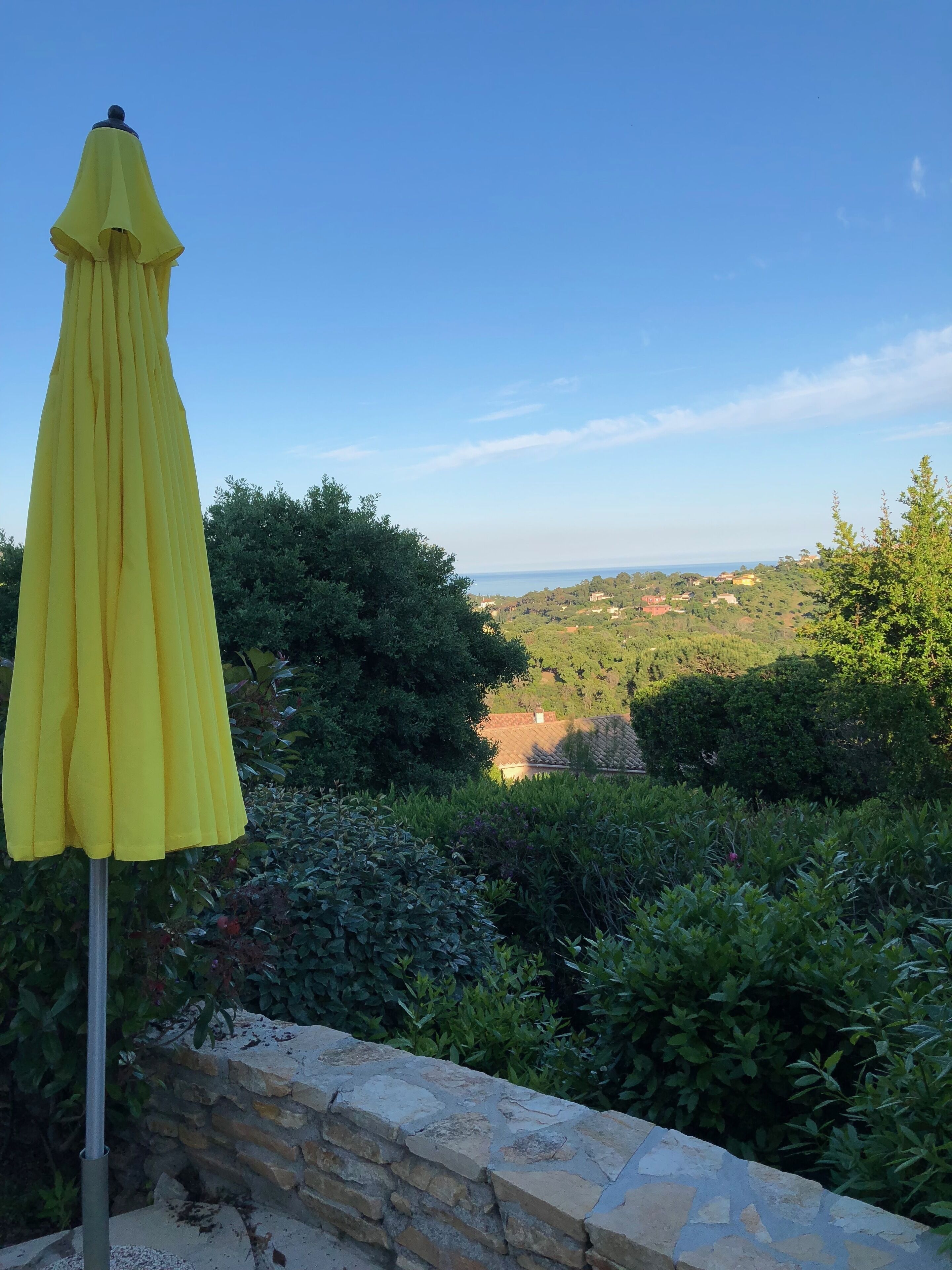 A yellow umbrella on a stone ledge overlooking a lush green landscape with a clear blue sky.