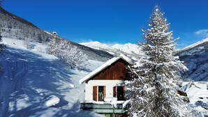 Une cabane en bois, dotée d’un toit en pente, entourée d’arbres et de montagnes couverts de neige.