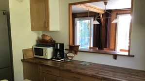 Une cuisine avec des meubles en bois, un four à micro-ondes, une machine à café et une fenêtre donnant sur un paysage verdoyant.