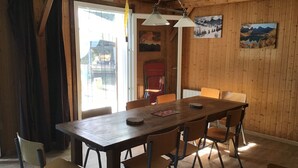 Un coin repas avec une table et des chaises en bois, un luminaire suspendu et une vue à travers une porte vitrée.