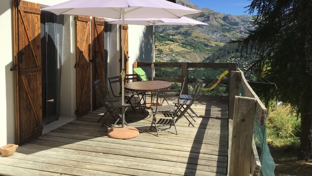 Une terrasse en bois avec une table et des chaises, un parasol blanc et une vue sur les montagnes.