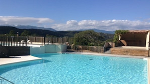 A clear blue swimming pool with a wooden deck, surrounded by a wooden fence and a stone wall. - Walk-new in charming residence with 300m² swimming pool in Porto Vecchio (Porto-Vecchio)